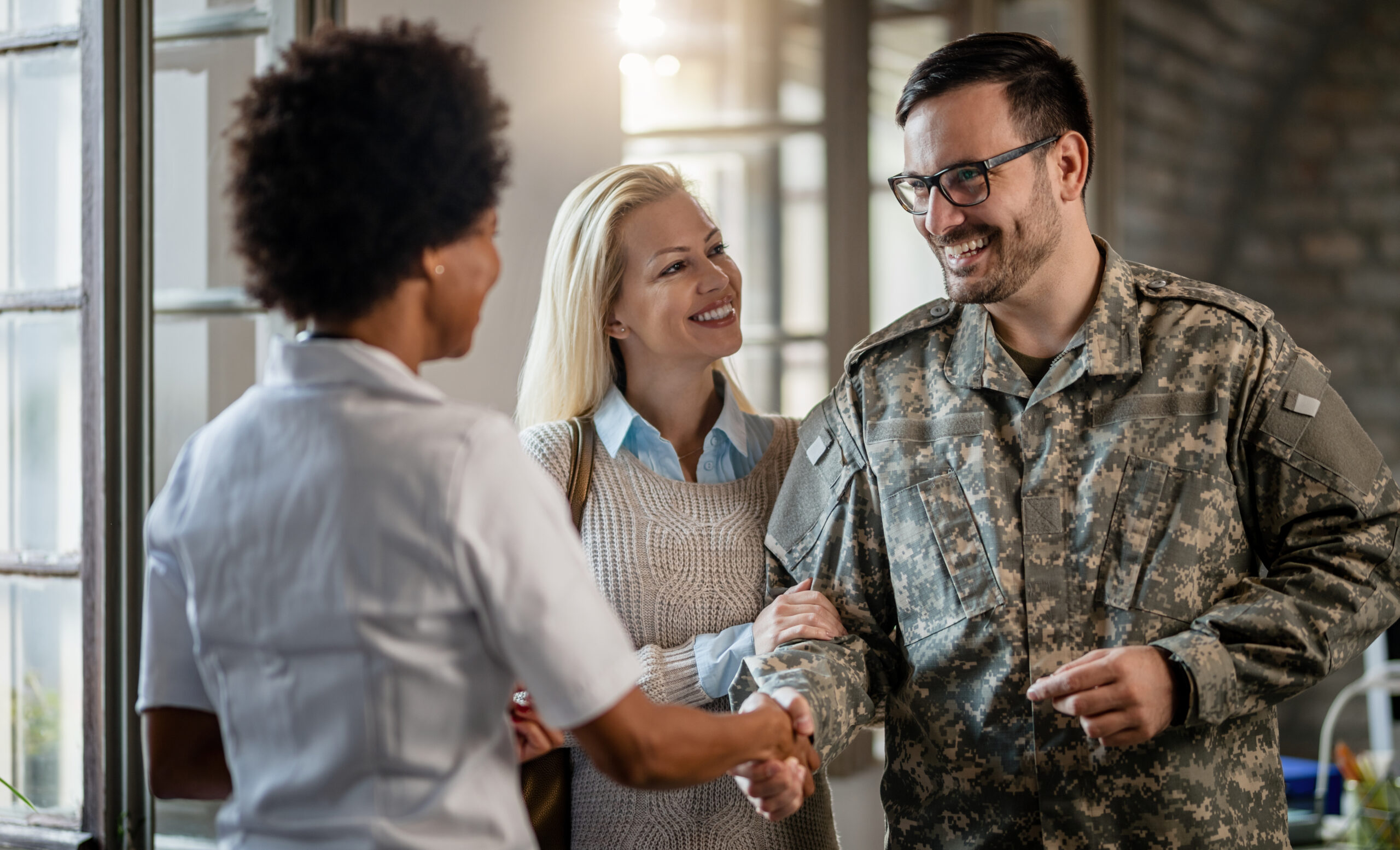 Happy,Military,Man,Shaking,Hands,With,Female,Doctor,While,Being Happy military man shaking hands with female doctor while being with his wife at medical counselling.
